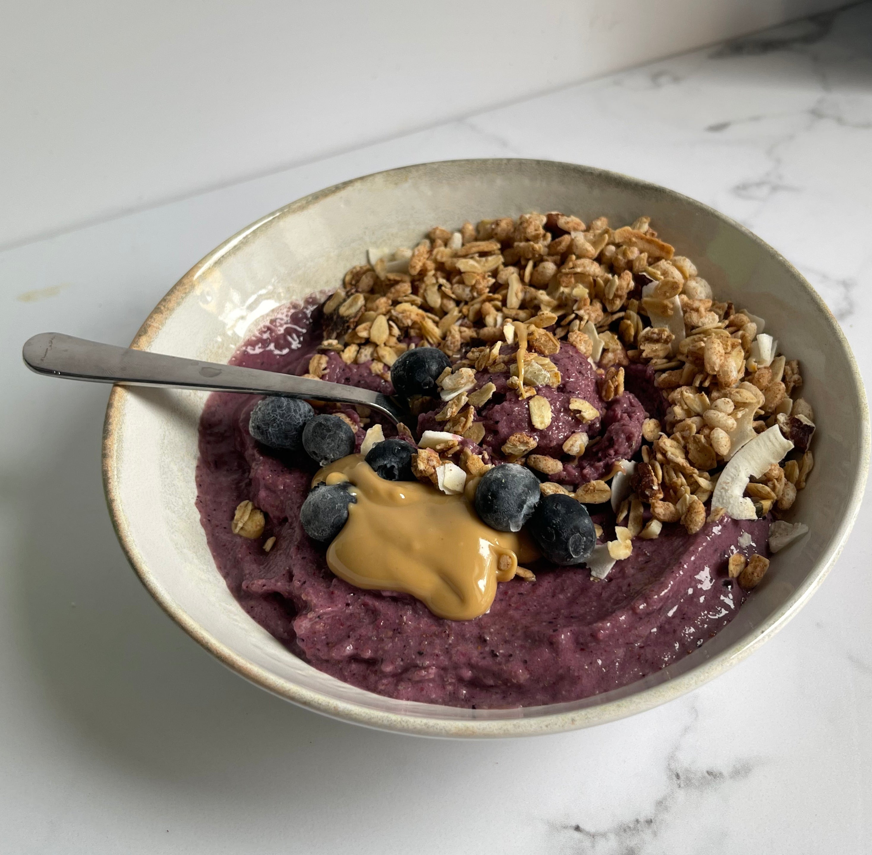 Piatto con smoothie bowl, con mirtilli, original granola, burro di arachidi, con cucchiaio argento