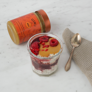 Barattolo protein power e bicchiere con overnight oat con crema di arachidi e lamponi, cucchiaino argento su panno da cucina 